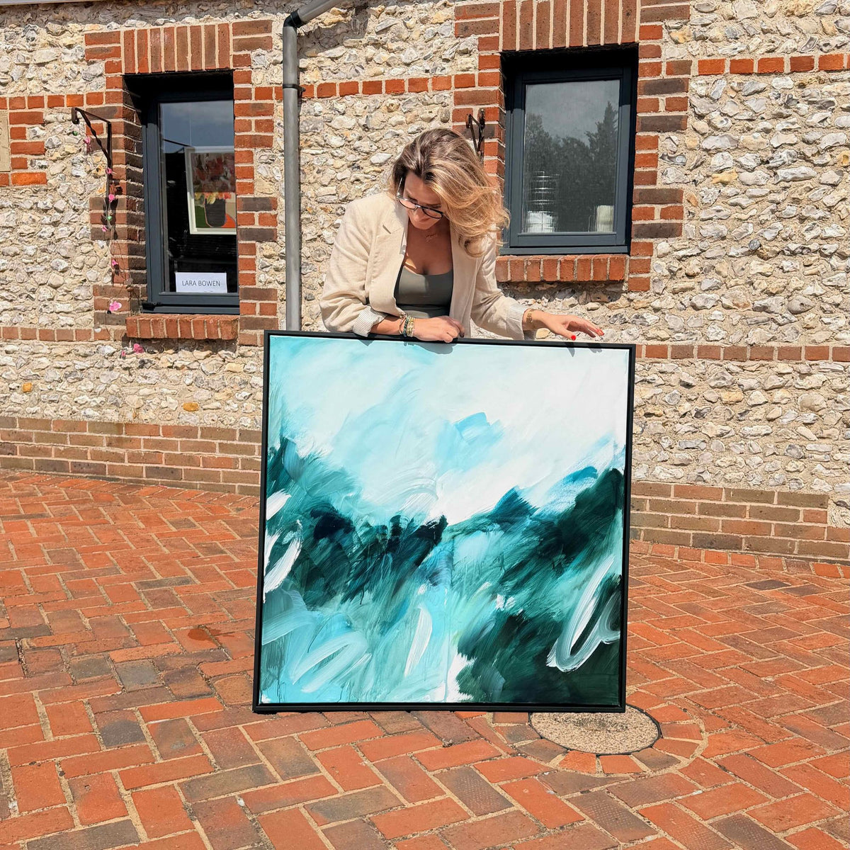 Joanna Gilbert holding Beneath the Surface, her original abstract painting in teal, blue-green and cream